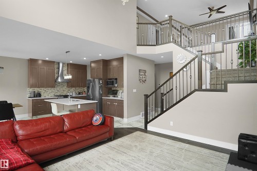 Open-concept living area featuring dark wood-finish flooring, a contemporary kitchen with brown cabinetry and light backsplash, a center island with seating, stainless steel appliances, and a multi-level staircase with dark wood handrails and balusters - 6108 173 Ave, Edmonton, AB 