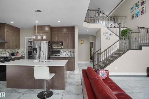 Open concept living space featuring a central kitchen island with seating, dark wood-finish cabinetry, stainless steel appliances, and mosaic tile backsplash - 6108 173 Ave, Edmonton, AB 