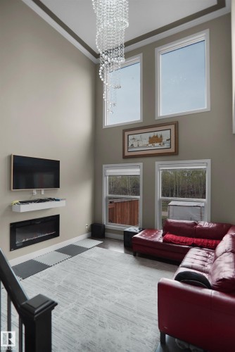 Double-height living space featuring a cascading chandelier, multiple large windows, an integrated electric fireplace, and a wall-mounted media console - 6108 173 Ave, Edmonton, AB 