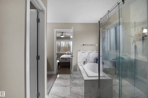 Bathroom featuring a built-in soaking tub, a frameless glass shower enclosure with a sliding door, and marble-look tile flooring - 6108 173 Ave, Edmonton, AB 