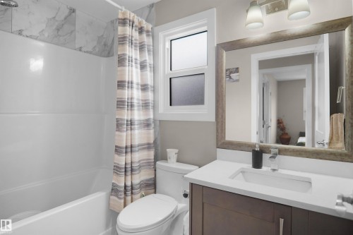 Bathroom featuring a white bathtub, marble-finish wall tiling, a vanity with a white countertop, a rectangular undermount sink, and an overhead vanity light fixture - 6108 173 Ave, Edmonton, AB 