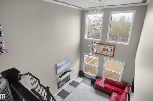 Two-story living area featuring a prominent spiral crystal chandelier, multiple large windows, and a built-in electric fireplace with a mantel shelf - 6108 173 Ave, Edmonton, AB 