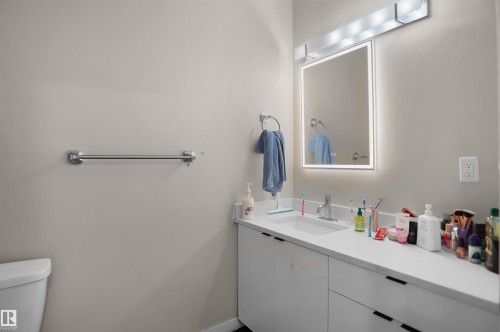 Bathroom featuring a white vanity with integrated sink, rectangular illuminated mirror, white countertop, and brushed nickel hardware - 6108 173 Ave, Edmonton, AB 
