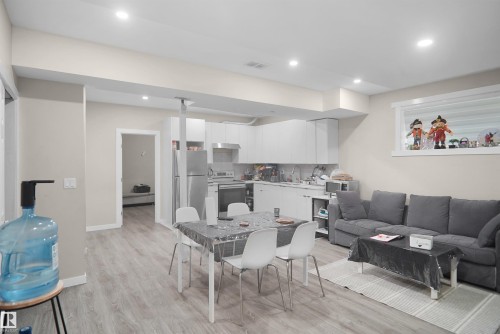 Open-concept living area featuring light wood-finish flooring, recessed lighting, and a kitchen with white cabinetry and stainless steel appliances - 6108 173 Ave, Edmonton, AB 
