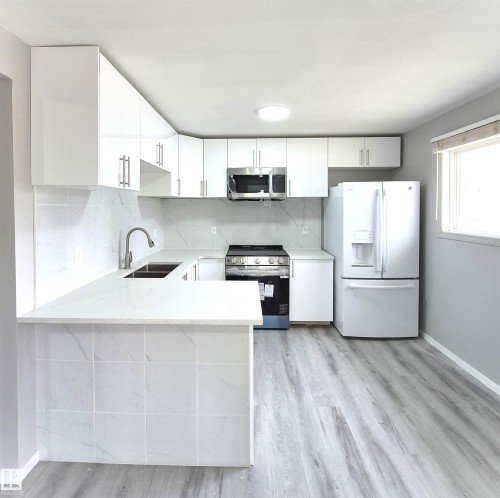 Kitchen featuring new white cabinetry, new countertops, new tile backsplash, new stainless over-the-range microwave, new electric stove, new dishwasher and LVP flooring. - 1312 Lakewood Road W, Edmonton, AB - Indoor Photo Showing Kitchen With Double Sink