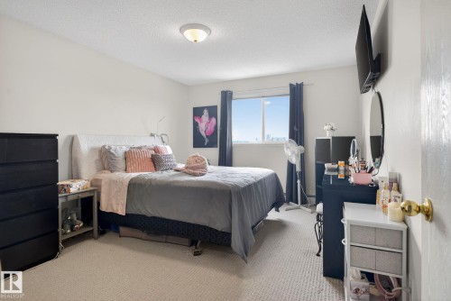 This room features light-colored carpeting, a window with dark curtains, and a ceiling light fixture - 423 2430 Guardian Road, Edmonton, AB - Indoor Photo Showing Bedroom