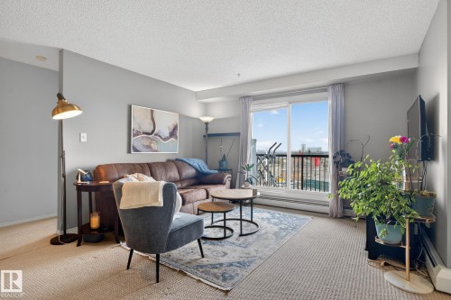 The living area features light-colored carpeting and provides access to an outdoor balcony through sliding glass doors - 423 2430 Guardian Road, Edmonton, AB - Indoor Photo Showing Living Room