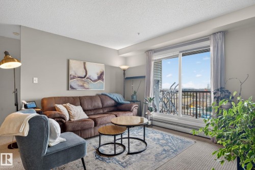 Living area featuring a sliding glass door providing natural light and access to a balcony, light grey walls, and a patterned area rug over carpet flooring - 423 2430 Guardian Road, Edmonton, AB - Indoor Photo Showing Living Room