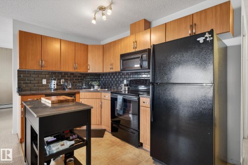 The kitchen features wood cabinetry, black subway tile backsplash, and black appliances including a refrigerator, microwave, and range - 423 2430 Guardian Road, Edmonton, AB - Indoor Photo Showing Kitchen