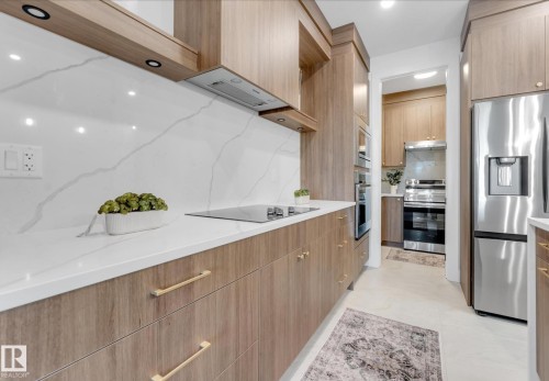 Kitchen featuring wood-finish cabinetry with gold-tone hardware, white countertops, and a full-height white backsplash - 4727 17 Avenue, Edmonton, AB - Indoor Photo Showing Kitchen With Upgraded Kitchen