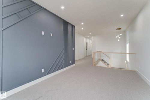 Spacious interior featuring a decorative accent wall with geometric molding, recessed lighting, and light-toned carpeting - 4727 17 Avenue, Edmonton, AB 
