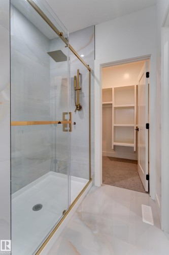 Contemporary shower enclosure featuring a frameless glass door with gold-toned hardware, a rain showerhead, and a handheld shower fixture - 4727 17 Avenue, Edmonton, AB 