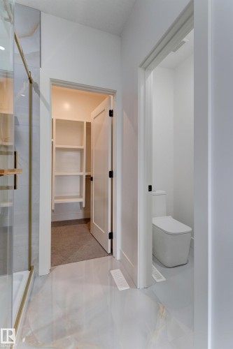 Modern bathroom with light-toned, veined flooring, a frameless glass shower enclosure with gold-tone accents, and a contemporary toilet - 4727 17 Avenue, Edmonton, AB 