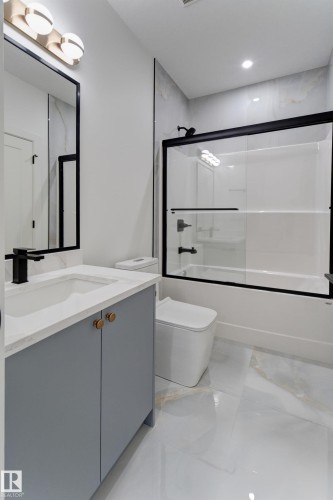 Contemporary bathroom featuring a grey vanity with a quartz countertop and integrated sink, matte black faucet, and rectangular mirror - 4727 17 Avenue, Edmonton, AB 