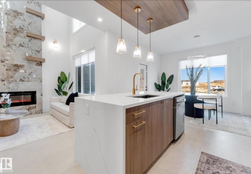 Modern kitchen island featuring a waterfall countertop, integrated sink with a gold-tone faucet, and wood-finish cabinetry - 4727 17 Avenue, Edmonton, AB - Indoor Photo Showing Kitchen With Fireplace With Upgraded Kitchen