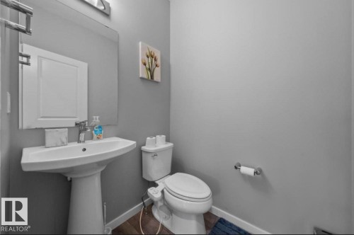Pedestal sink with chrome faucet, mirror, wall-mounted light fixture, toilet, and wood-finish flooring - 243 39 Avenue Nw, Edmonton, AB - Indoor Photo Showing Bathroom