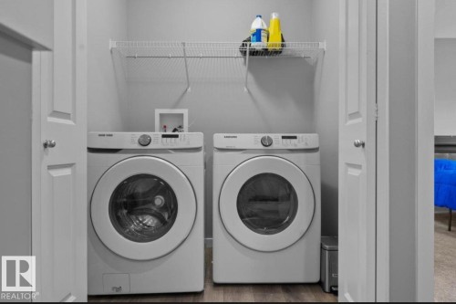 Dedicated laundry area featuring a front-loading washer and dryer set, wire shelving for storage, and wood-finish flooring - 243 39 Avenue Nw, Edmonton, AB - Indoor Photo Showing Laundry Room