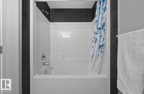 Bathtub and shower combination featuring a white surround and dark grey wall tiling, complete with a chrome showerhead and faucet - 243 39 Avenue Nw, Edmonton, AB - Indoor Photo Showing Bathroom