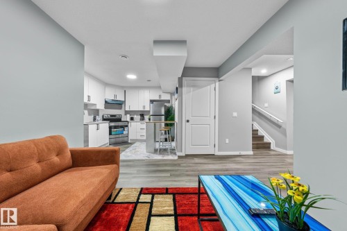 Open-concept living area featuring wood-finish flooring, recessed lighting, a modern kitchen with white cabinetry and stainless steel appliances, and a staircase with a white handrail - 243 39 Avenue Nw, Edmonton, AB - Indoor Photo Showing Living Room