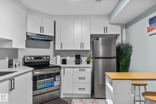 Kitchen featuring white cabinetry with dark pulls, stainless steel appliances, a range hood, and light-toned countertops - 243 39 Avenue Nw, Edmonton, AB - Indoor Photo Showing Kitchen With Stainless Steel Kitchen