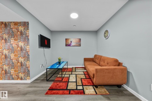 Spacious room featuring wood-finish flooring, light gray walls, and a distinctive accent wall with a building motif - 243 39 Avenue Nw, Edmonton, AB - Indoor