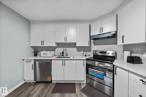 Kitchen featuring white cabinetry, light-toned countertops, stainless steel appliances, and wood-finish flooring - 243 39 Avenue Nw, Edmonton, AB - Indoor Photo Showing Kitchen With Stainless Steel Kitchen