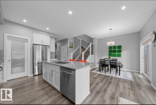 Spacious kitchen and dining area featuring a central island with an integrated sink, stainless steel appliances, white cabinetry, wood-finish flooring, and recessed lighting - 243 39 Avenue Nw, Edmonton, AB - Indoor Photo Showing Kitchen With Stainless Steel Kitchen With Double Sink