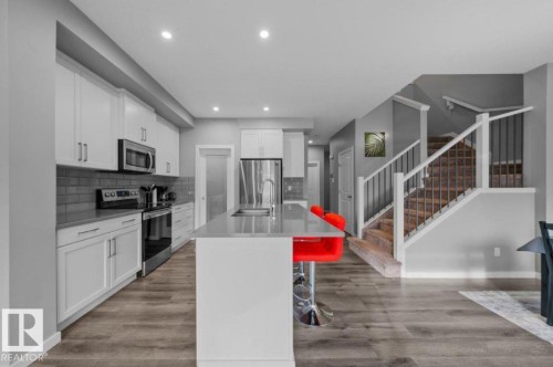 Modern kitchen featuring a large center island with a stainless steel sink, sleek white cabinetry, stainless steel appliances, and a gray subway tile backsplash - 243 39 Avenue Nw, Edmonton, AB - Indoor Photo Showing Kitchen With Stainless Steel Kitchen With Double Sink With Upgraded Kitchen
