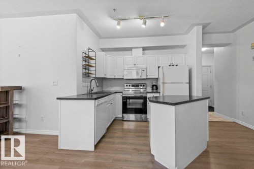 Kitchen featuring white cabinetry, dark countertops, stainless steel appliances, and wood-finish flooring - 304 10011 110 Street, Edmonton, AB - Indoor Photo Showing Kitchen