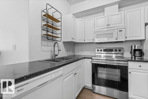 Kitchen featuring white cabinetry, dark countertops, a stainless steel range, a built-in microwave, and a double basin sink with a gooseneck faucet - 304 10011 110 Street, Edmonton, AB - Indoor Photo Showing Kitchen With Double Sink