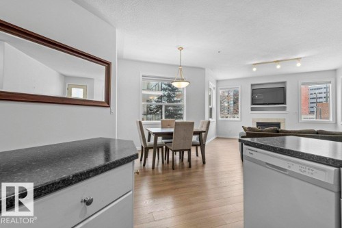 Open-concept living area featuring wood-finish flooring, a built-in fireplace, multiple windows, and a dining space with pendant lighting - 304 10011 110 Street, Edmonton, AB - Indoor
