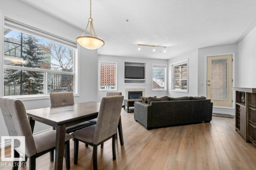Open-concept living space featuring wood-finish flooring, a dining area with an overhead light fixture, and a living area with a built-in media center above a fireplace - 304 10011 110 Street, Edmonton, AB - Indoor Photo Showing Dining Room With Fireplace