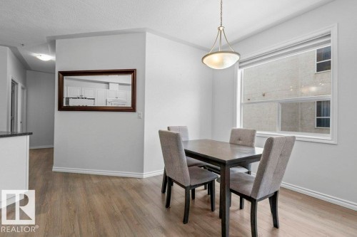 Dining area featuring wood-finish flooring, a contemporary pendant light fixture, and a large window with roller shades - 304 10011 110 Street, Edmonton, AB - Indoor Photo Showing Dining Room