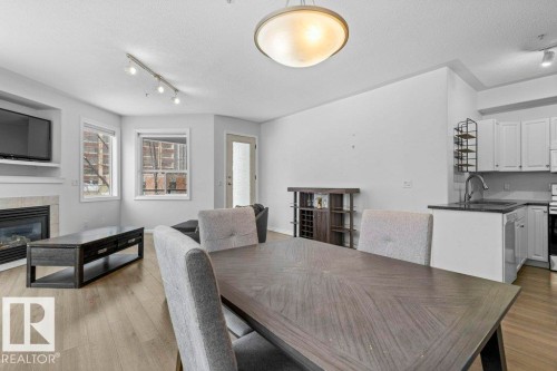Open-concept living area featuring light wood-finish flooring, a contemporary fireplace with a stone surround, and white cabinetry in the kitchen - 304 10011 110 Street, Edmonton, AB - Indoor With Fireplace