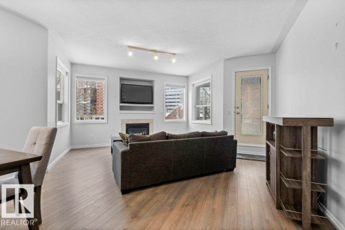 Open-concept living space with wood-finish flooring, a built-in media niche, and a fireplace with a light-toned surround - 304 10011 110 Street, Edmonton, AB - Indoor With Fireplace