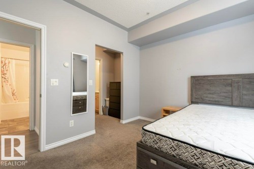 Carpeted room featuring a wood-finish bed frame with headboard, light gray painted walls, and white baseboards - 304 10011 110 Street, Edmonton, AB - Indoor Photo Showing Bedroom