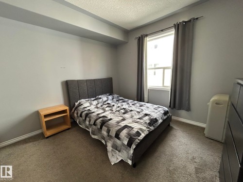 Carpeted room featuring a single window with curtain rods, light gray walls, and a textured ceiling - 304 10011 110 Street, Edmonton, AB - Indoor Photo Showing Bedroom
