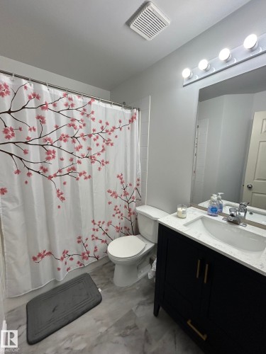 Bathroom featuring a dark wood-finish vanity with gold-tone hardware, a white countertop with an integrated sink, a wall-mounted light fixture, and marble-look floor tiles - 304 10011 110 Street, Edmonton, AB - Indoor Photo Showing Bathroom