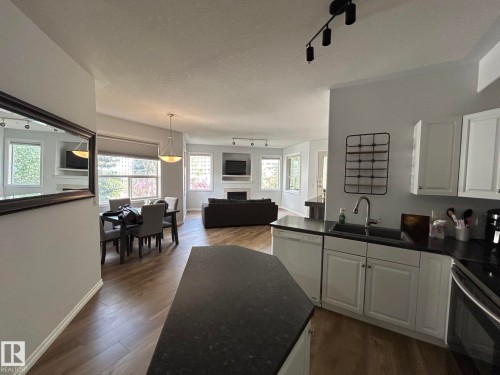 Kitchen featuring white cabinetry, dark countertops, and a stainless steel sink with a modern faucet - 304 10011 110 Street, Edmonton, AB - Indoor Photo Showing Kitchen