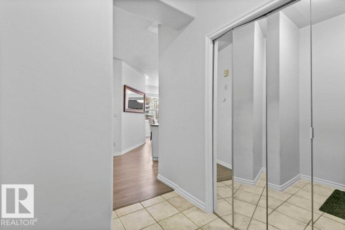 Entryway featuring ceramic tile flooring, mirrored bi-fold closet doors, and wood-finish flooring extending into the interior - 304 10011 110 Street, Edmonton, AB - Indoor Photo Showing Other Room