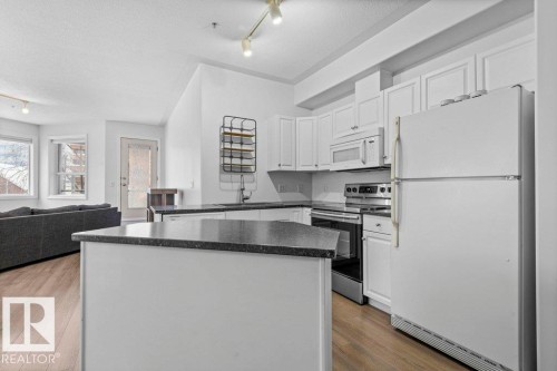 Kitchen with white cabinetry, dark countertops, and wood-finish flooring - 304 10011 110 Street, Edmonton, AB - Indoor Photo Showing Kitchen