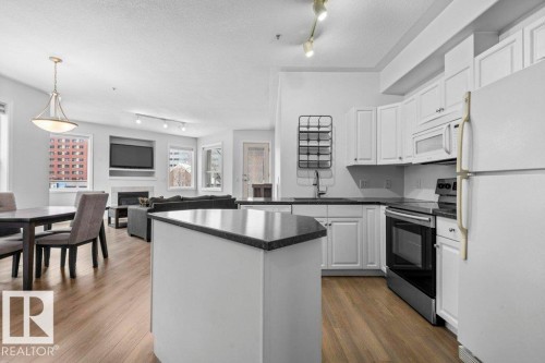Modern kitchen featuring white cabinetry, dark countertops, and stainless steel appliances - 304 10011 110 Street, Edmonton, AB - Indoor Photo Showing Kitchen With Upgraded Kitchen