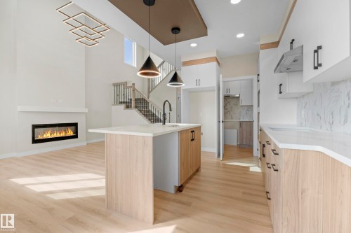 Open-concept living space featuring a modern linear fireplace and light wood-finish flooring - 4915 17 Avenue, Edmonton, AB - Indoor Photo Showing Kitchen With Fireplace
