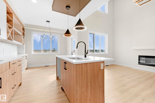 Modern kitchen featuring a central island with an undermount sink and matte black faucet, light wood-finish cabinetry, white countertops, and a full-height tile backsplash - 4915 17 Avenue, Edmonton, AB - Indoor Photo Showing Kitchen With Fireplace With Double Sink