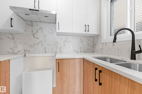 Contemporary kitchen featuring two-tone cabinetry with white upper and wood-finish lower cabinets, complemented by black hardware - 4915 17 Avenue, Edmonton, AB - Indoor Photo Showing Kitchen With Double Sink