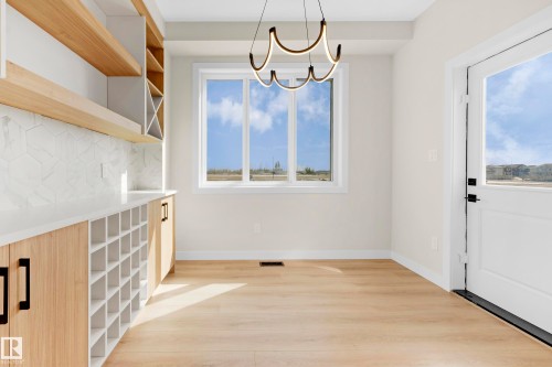 Modern interior with light wood-finish flooring, featuring a large window, a sleek pendant light fixture, built-in cabinetry with natural wood-finish doors, and a white hexagonal tile backsplash - 4915 17 Avenue, Edmonton, AB - Indoor Photo Showing Other Room