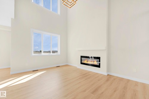 Expansive living space featuring a linear electric fireplace, high ceilings, large windows, wood-finish flooring, and a contemporary light fixture - 4915 17 Avenue, Edmonton, AB - Indoor With Fireplace