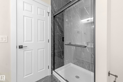 Shower enclosure with dark-framed glass door, black marble-patterned wall tiling, and a white shower pan - 4915 17 Avenue, Edmonton, AB - Indoor Photo Showing Bathroom