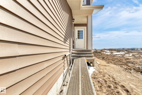 Side exterior featuring neutral-toned horizontal siding, a white entry door with divided lites, an overhead soffit, and a foundational ramp - 4915 17 Avenue, Edmonton, AB - Outdoor