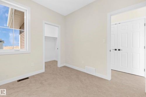 Neutral-toned carpeted room featuring a white-framed window, a recessed open closet, and white bi-fold doors - 4915 17 Avenue, Edmonton, AB - Indoor Photo Showing Other Room